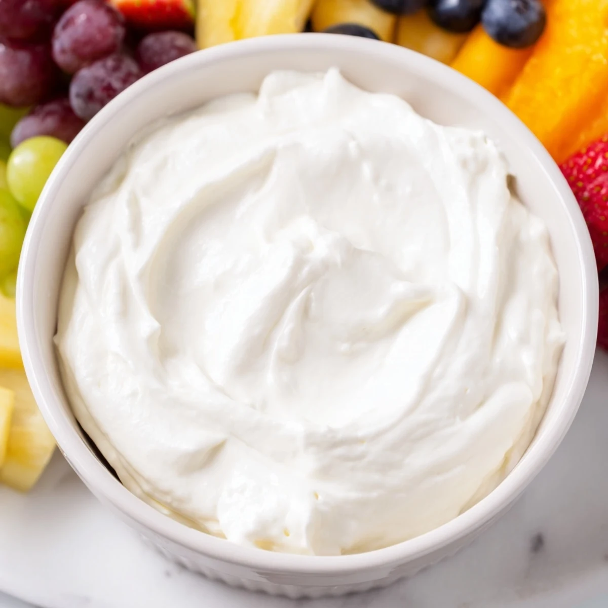 Creamy cream cheese fruit dip in a bowl surrounded by colorful, vibrant fresh berries.