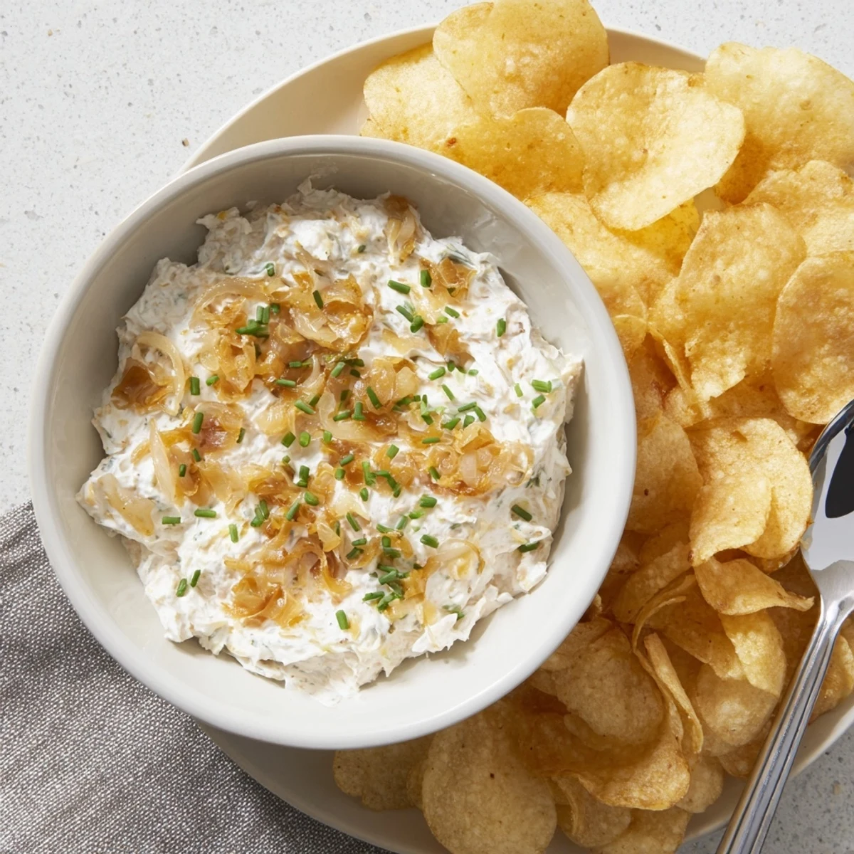 Golden potato chips arranged around a bowl of creamy, homemade onion dip for sharing.