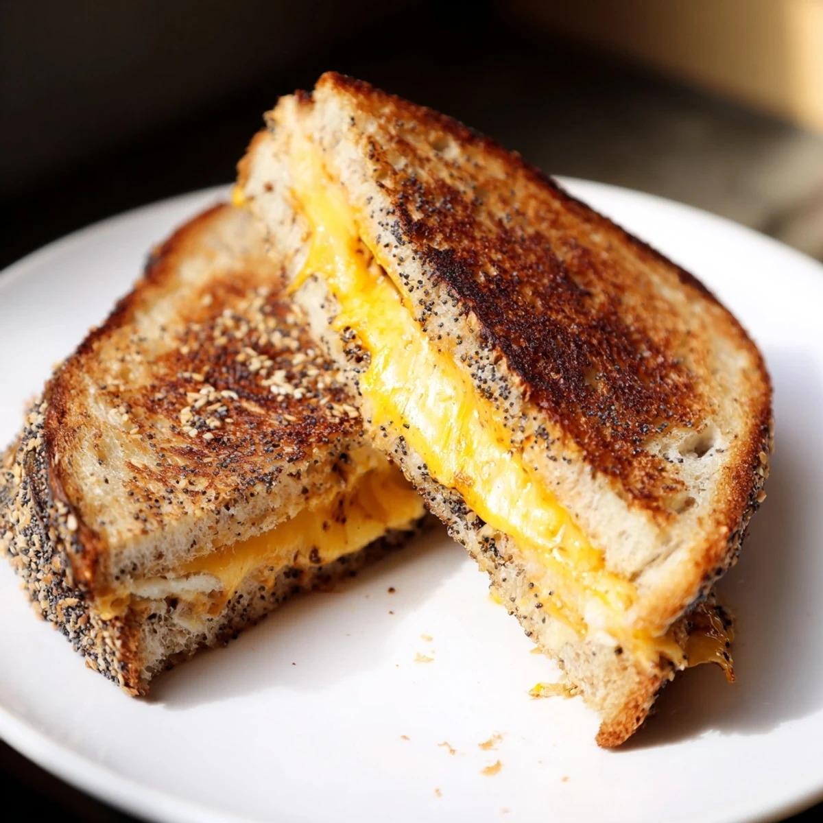 Crispy-edged everything bagel grilled cheese on a plate, ready to be cut and enjoyed with tomato soup.