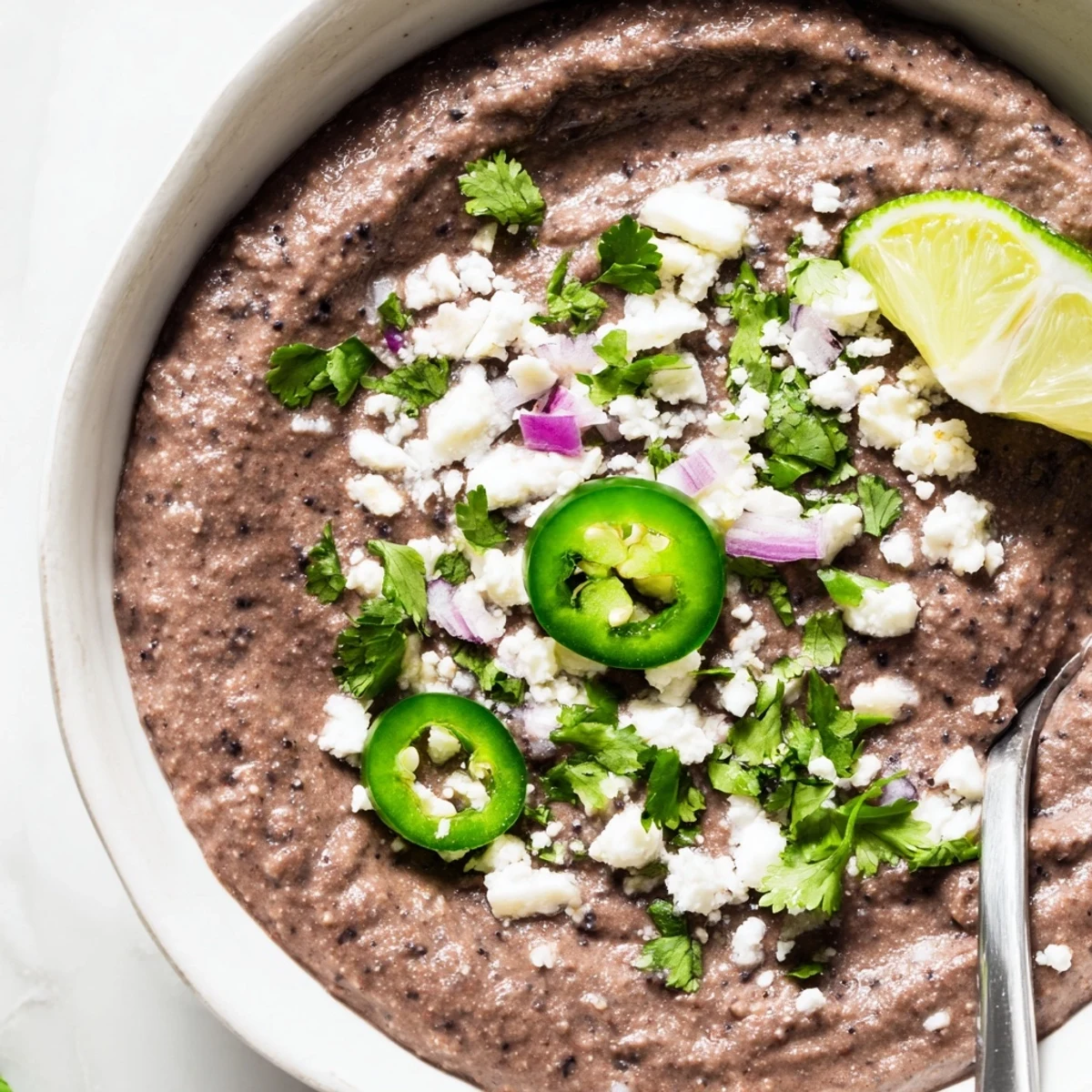 Creamy Spicy Black Bean Dip in a rustic bowl, topped with crumbled feta and sliced jalapeños for parties.  