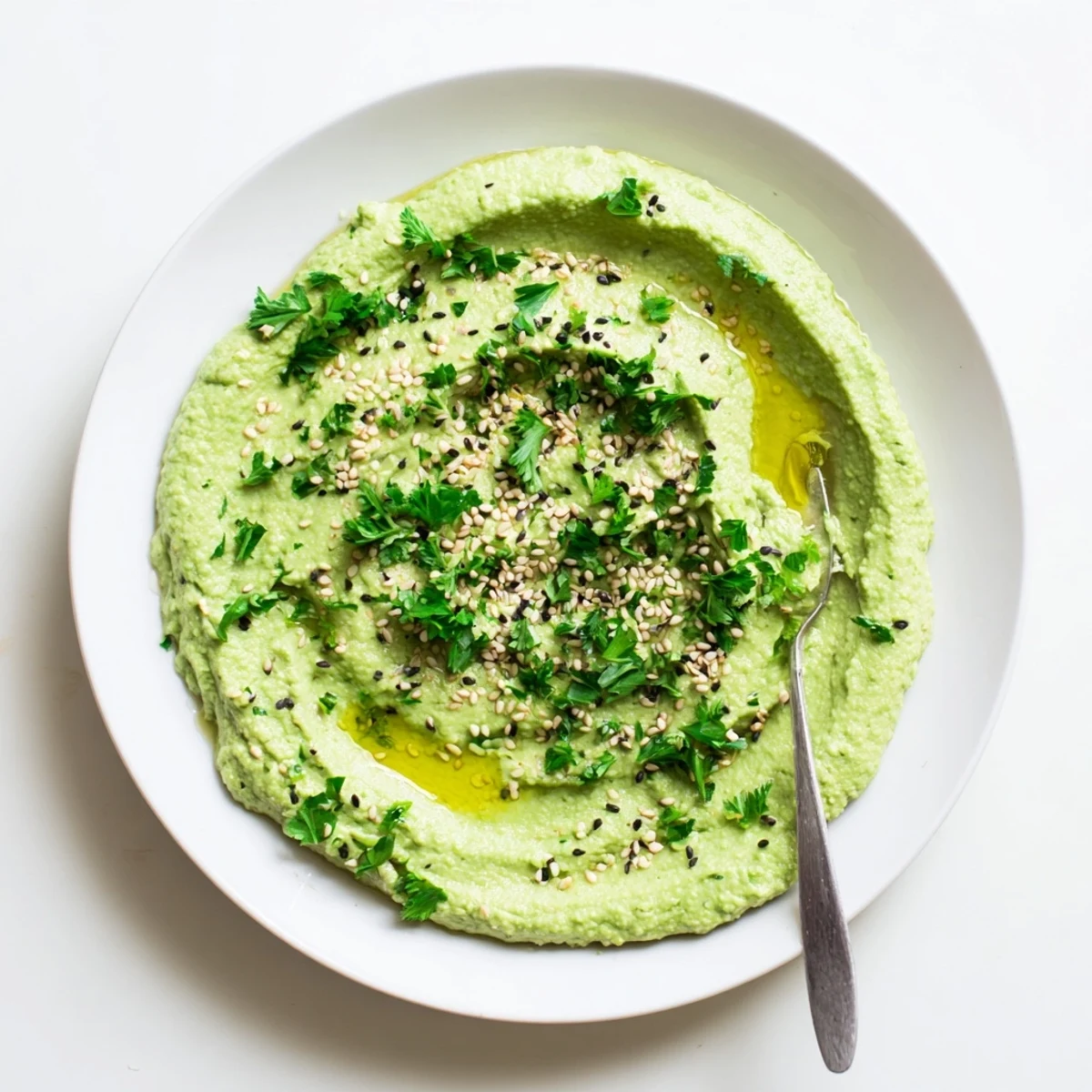 A vibrant bowl of homemade Edamame Hummus topped with olive oil and toasted sesame seeds, ready for dipping with fresh veggies.