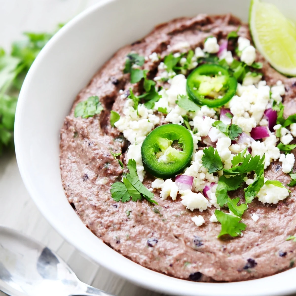 A vibrant bowl of Spicy Black Bean Dip garnished with fresh cilantro and lime wedges for a zesty kick.  