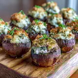 Perfectly baked Stuffed Asiago-Basil Mushrooms, filled with creamy cheese and basil, arranged on a rustic wooden board.