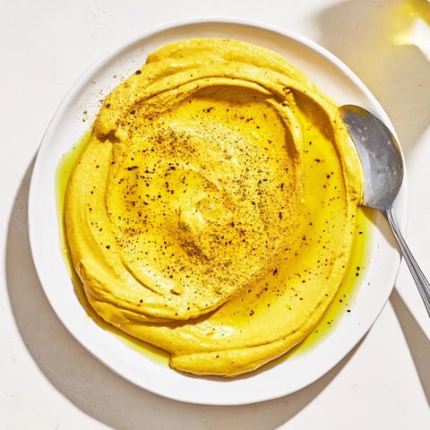 A bowl of creamy, golden chickpea curry paste garnished with a drizzle of olive oil and curry powder.