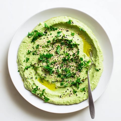 A vibrant bowl of homemade Edamame Hummus topped with olive oil and toasted sesame seeds, ready for dipping with fresh veggies.