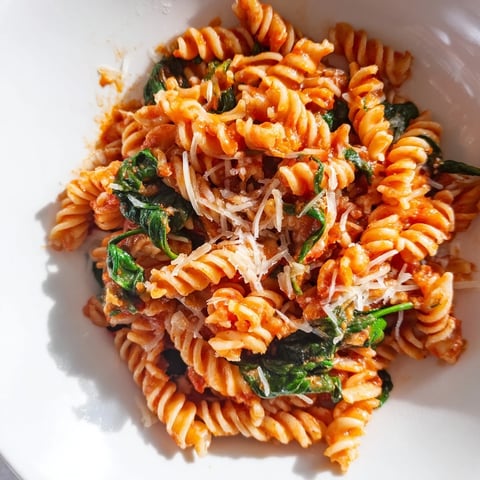 A vibrant bowl of Tomato Spinach One-Pot Rotini features tender rotini pasta tossed with juicy diced tomatoes and fresh wilted spinach leaves in a savory broth.