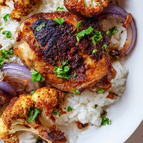 Golden roasted cauliflower florets and seasoned chicken thighs arranged on a sheet pan beside fluffy white rice and lemon wedges.  