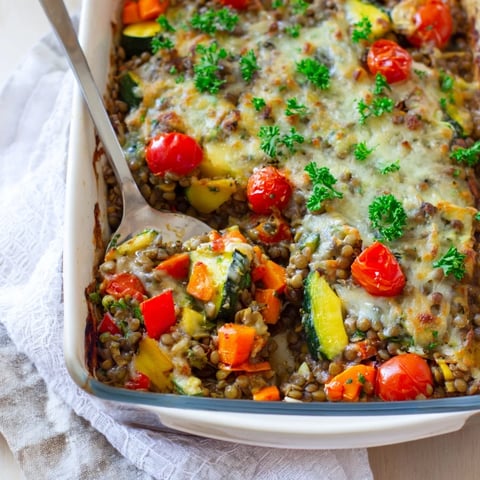 A close-up of a steaming Green Lentil and Vegetable Casserole, featuring tender lentils, diced carrots, and cherry tomatoes in a rich, bubbling sauce.