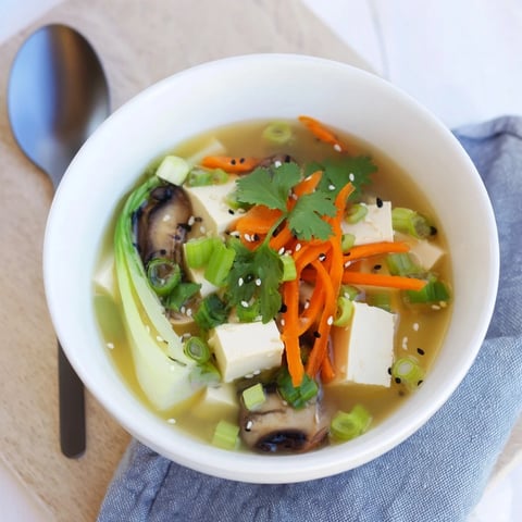 Silky tofu cubes and vibrant vegetables float in a steaming broth, featuring shiitake mushrooms and bok choy for a light, comforting Asian-inspired meal.