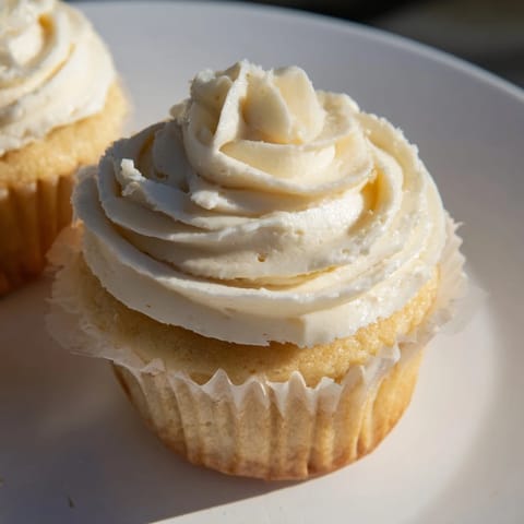 A close-up of beautifully frosted vanilla cupcakes, showing the moist cake and swirls of creamy frosting.