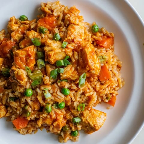 Golden fried rice with chunks of butter chicken and diced carrots, garnished with fresh green onions on a rustic plate.