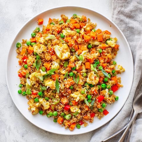 Scrambled eggs and fresh green onions top a serving of hot cauliflower fried rice, with a small dish of soy sauce nearby.  