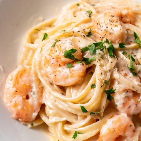 A close-up of Creamy Garlic Shrimp Pasta, garnished with parsley and lemon wedges on a rustic dinner plate.