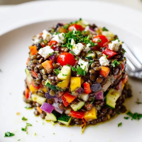 A healthy serving of Black Lentil Salad with Roasted Vegetables in a rustic white bowl, featuring fresh parsley and a zesty lemon dressing.