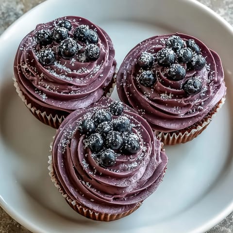 Vibrant black currant frosting swirls atop a cupcake, its deep purple hue hinting at tangy-sweet flavor and silky texture.
