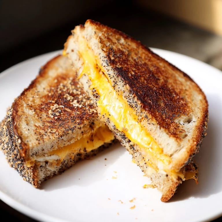 Crispy-edged everything bagel grilled cheese on a plate, ready to be cut and enjoyed with tomato soup.