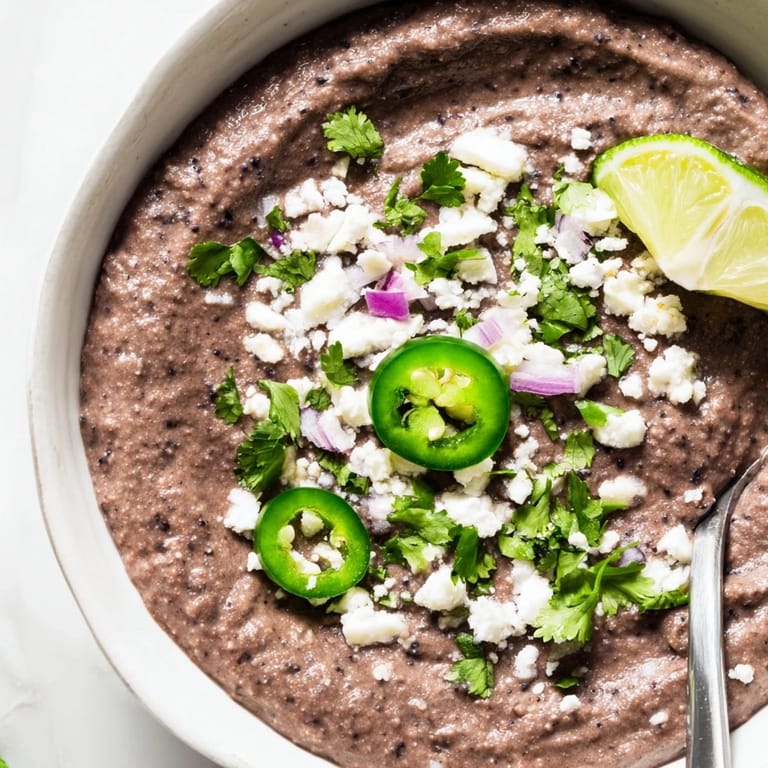 Creamy Spicy Black Bean Dip in a rustic bowl, topped with crumbled feta and sliced jalapeños for parties.  