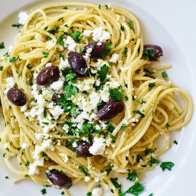 A close-up view of Greek Chicken Spaghetti shows sliced chicken, creamy feta, and a light lemon-oregano dressing glistening on pasta.