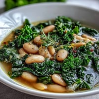 A steaming bowl of kale and white bean soup with bright lemon and garlic, garnished with fresh parsley.